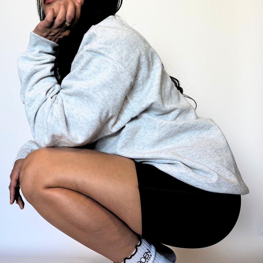 Person wearing a light gray sweatshirt and black shorts on a white background