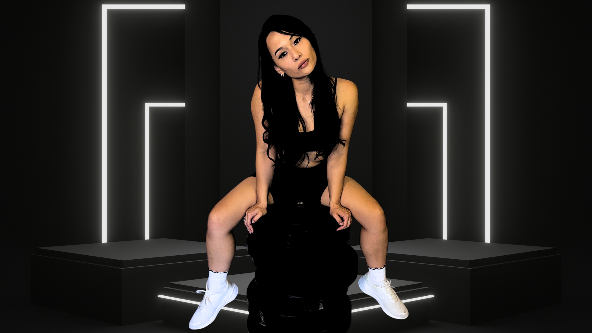 Woman sitting on a black stool against a dark background with neon lights.