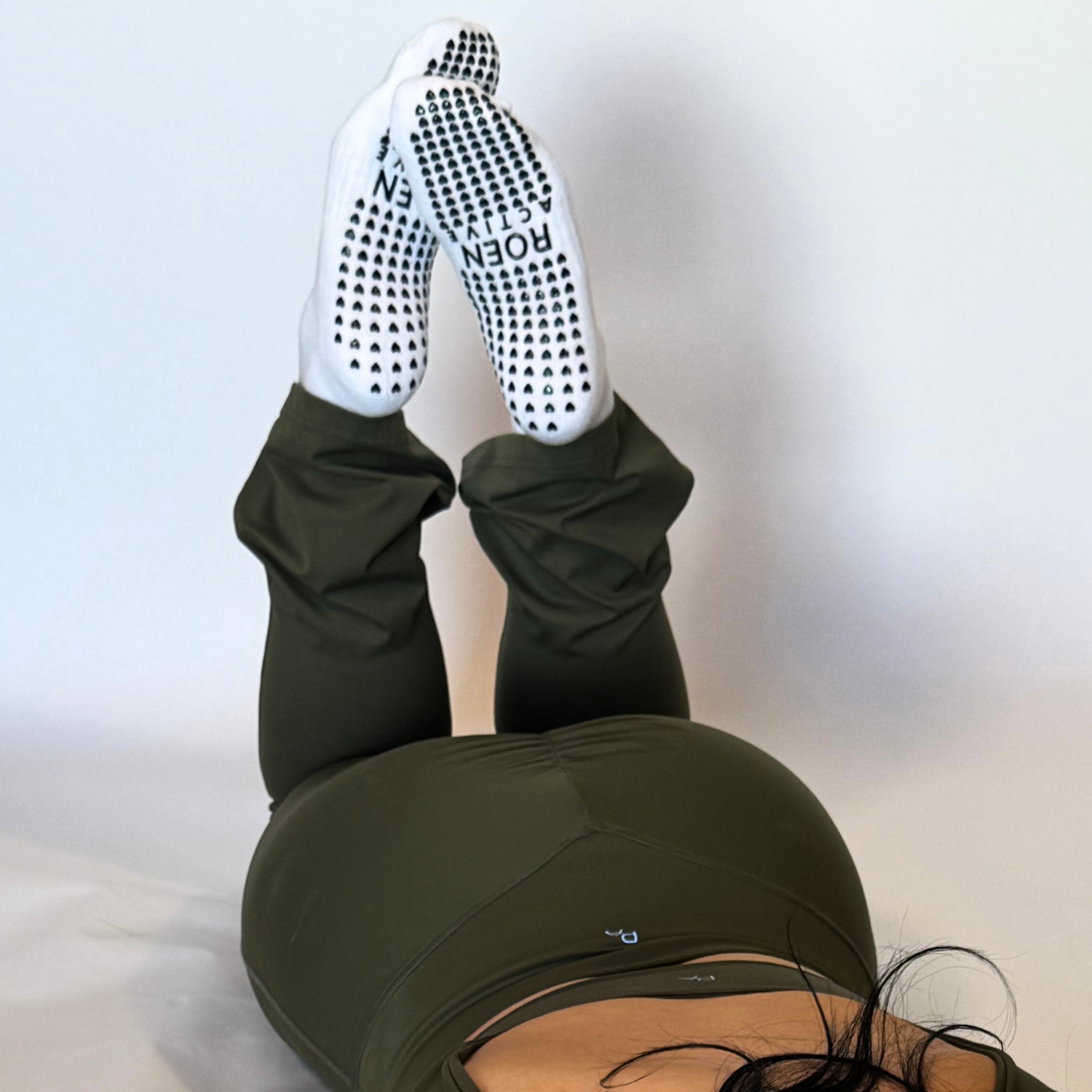 Person wearing green leggings and white socks with black dots on a light gray background